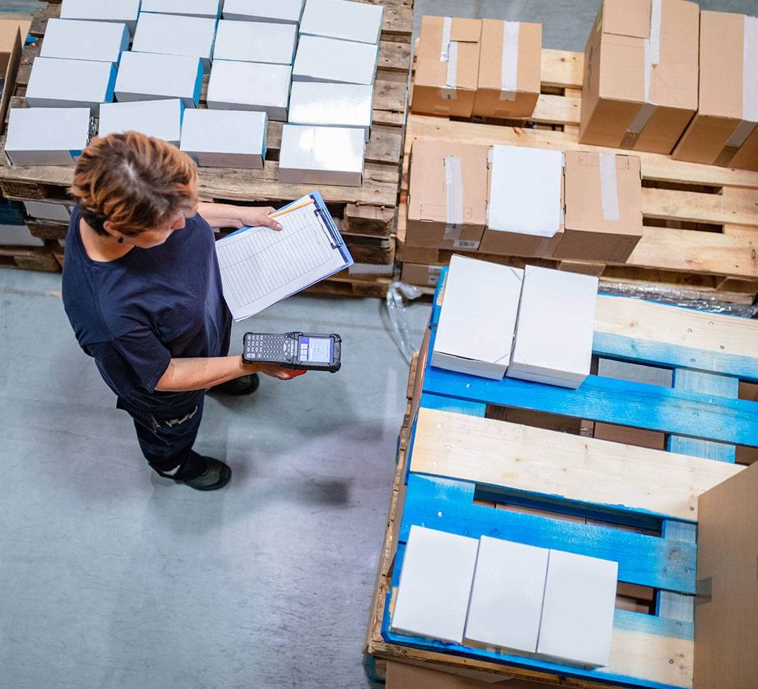 Worker scanning inventory with a handheld device in a warehouse area, emphasizing how security cameras can monitor stockrooms and prevent inventory shrinkage in retail stores.